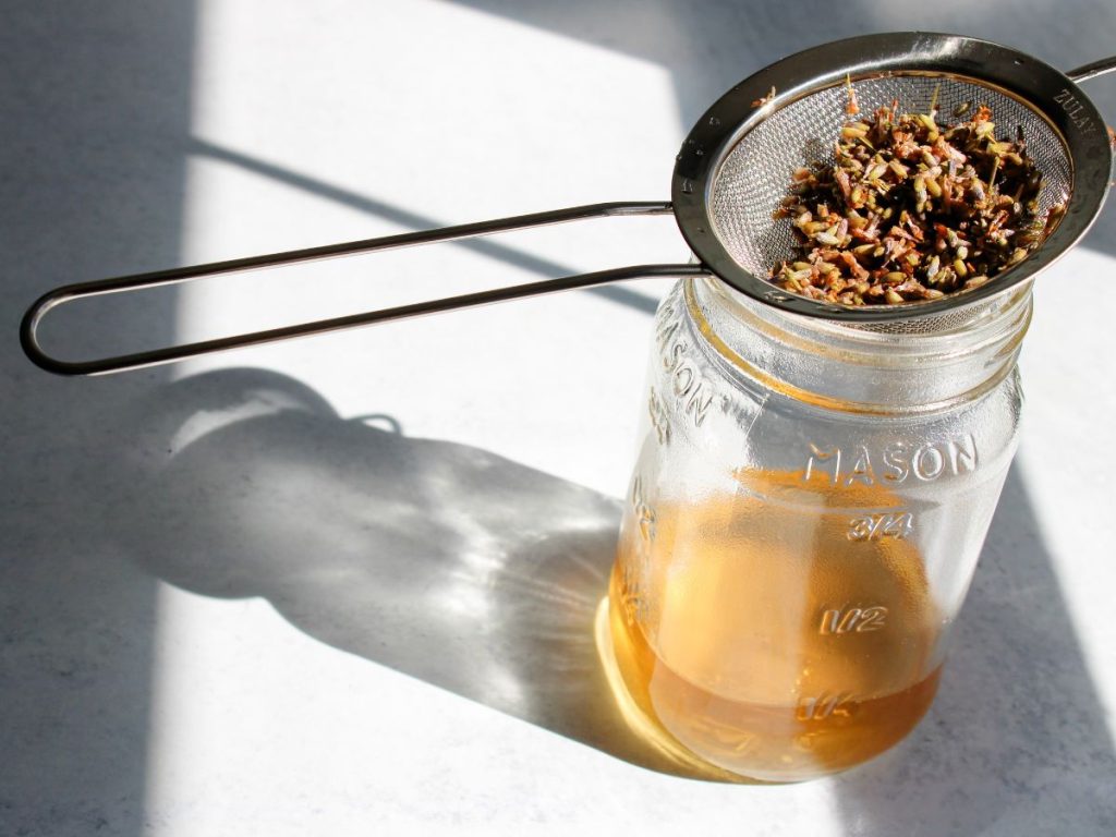 Lavender being strained out of tea with a small strainer and jar