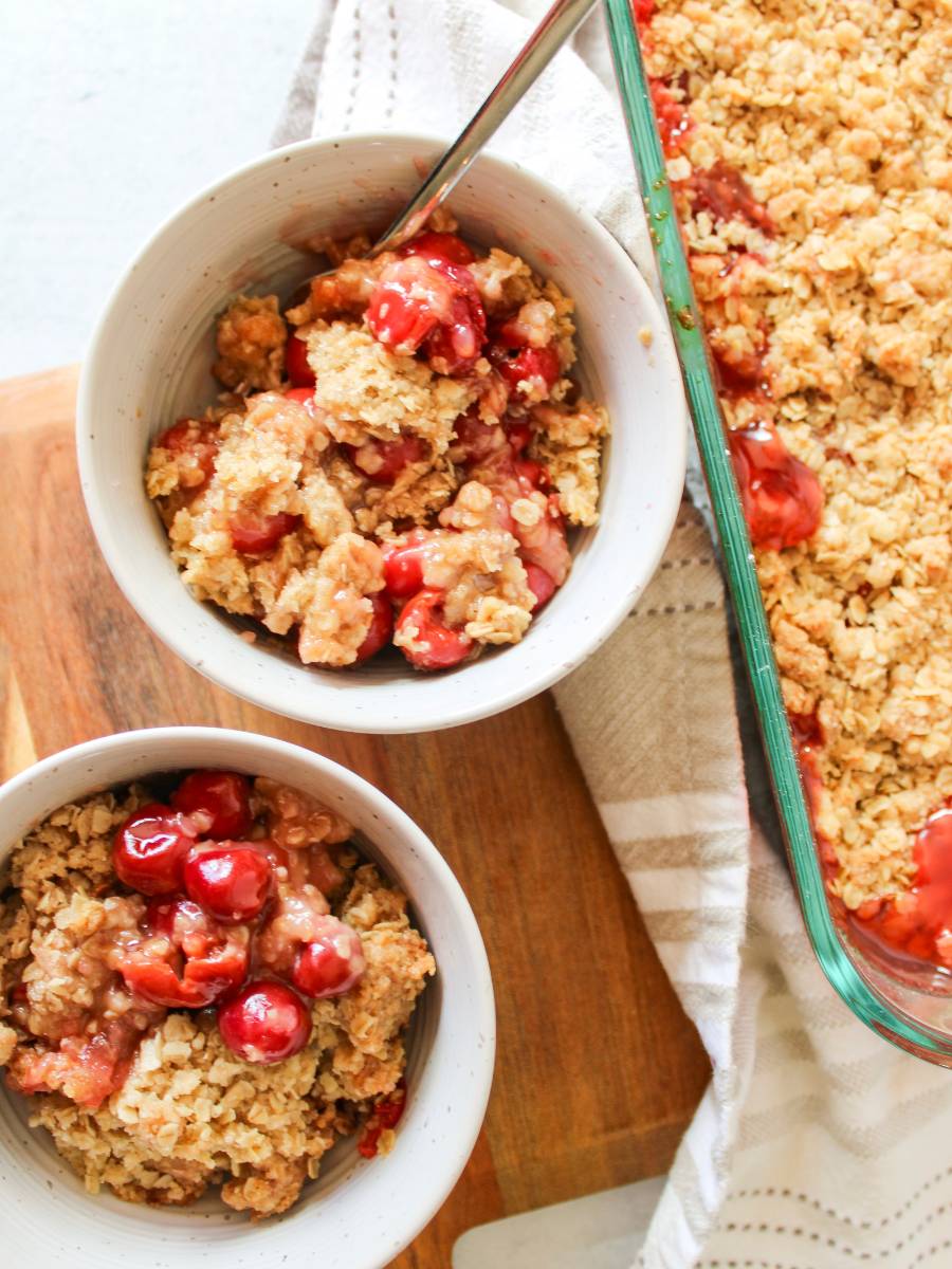 Two bowls of cherry crisp next to 9x13 pan