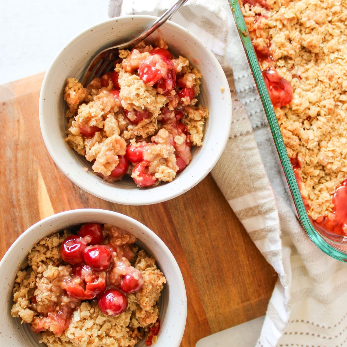 Two bowls next to a 9x13 pan filled with tart cherry crisp.