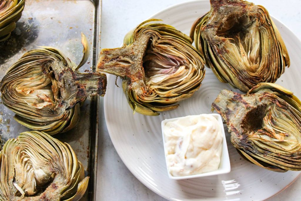 plate of grilled artichokes next to sheet pan