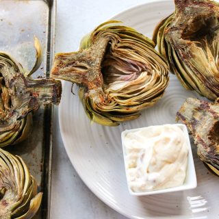 plate of grilled artichokes next to sheet pan