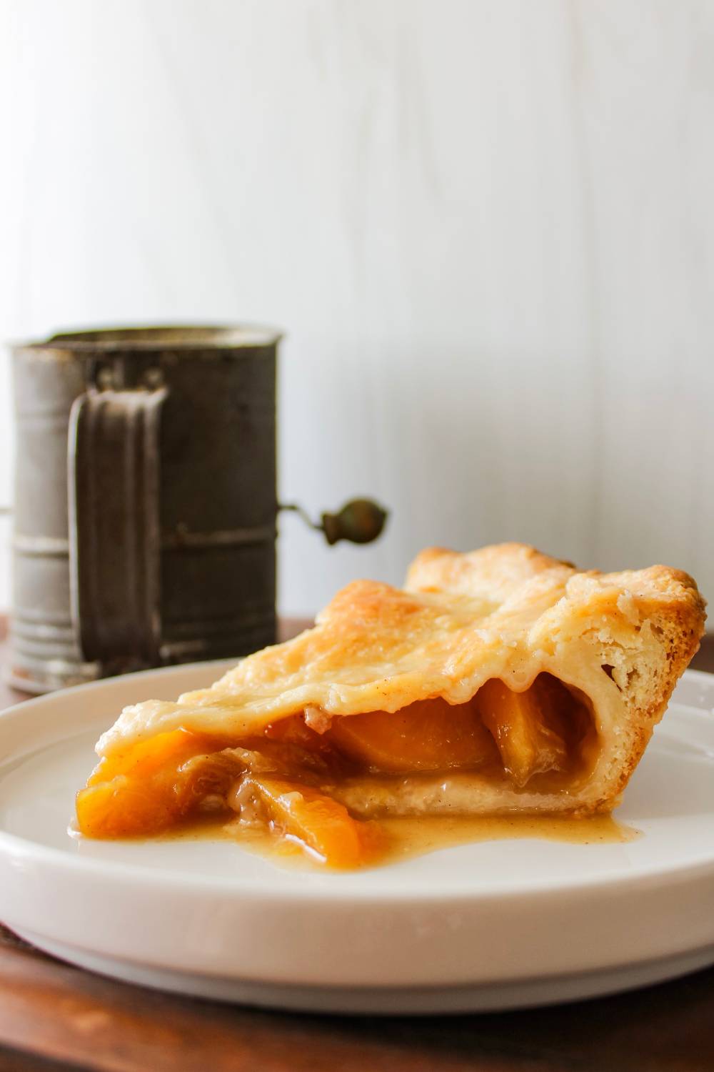 slice of peach pie next to flour sifter