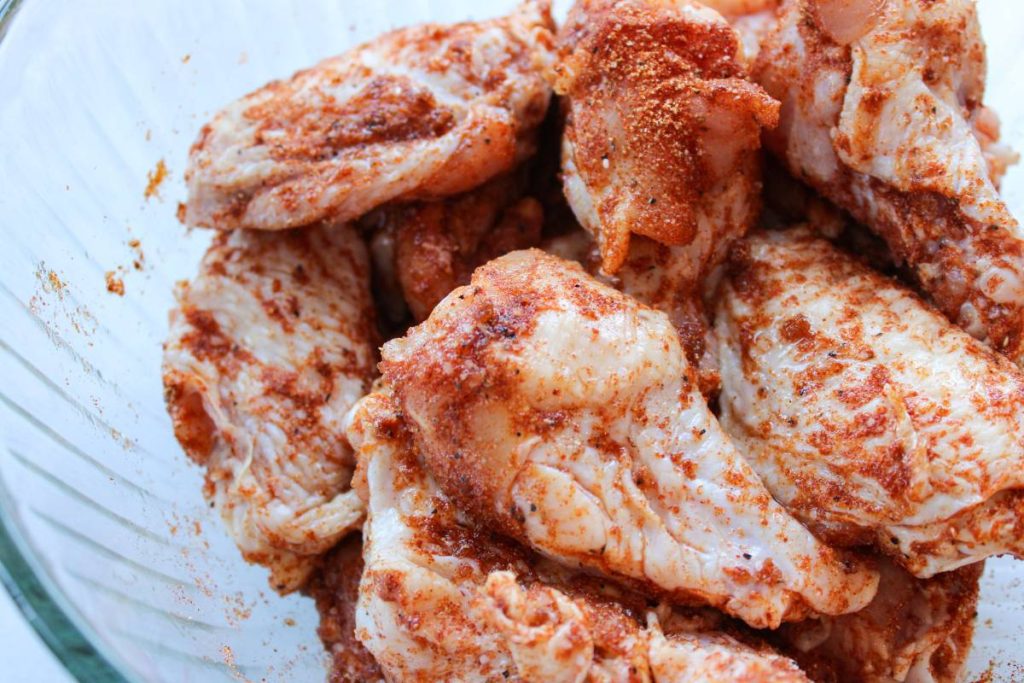 raw wings in a clear bowl with dry rub on top