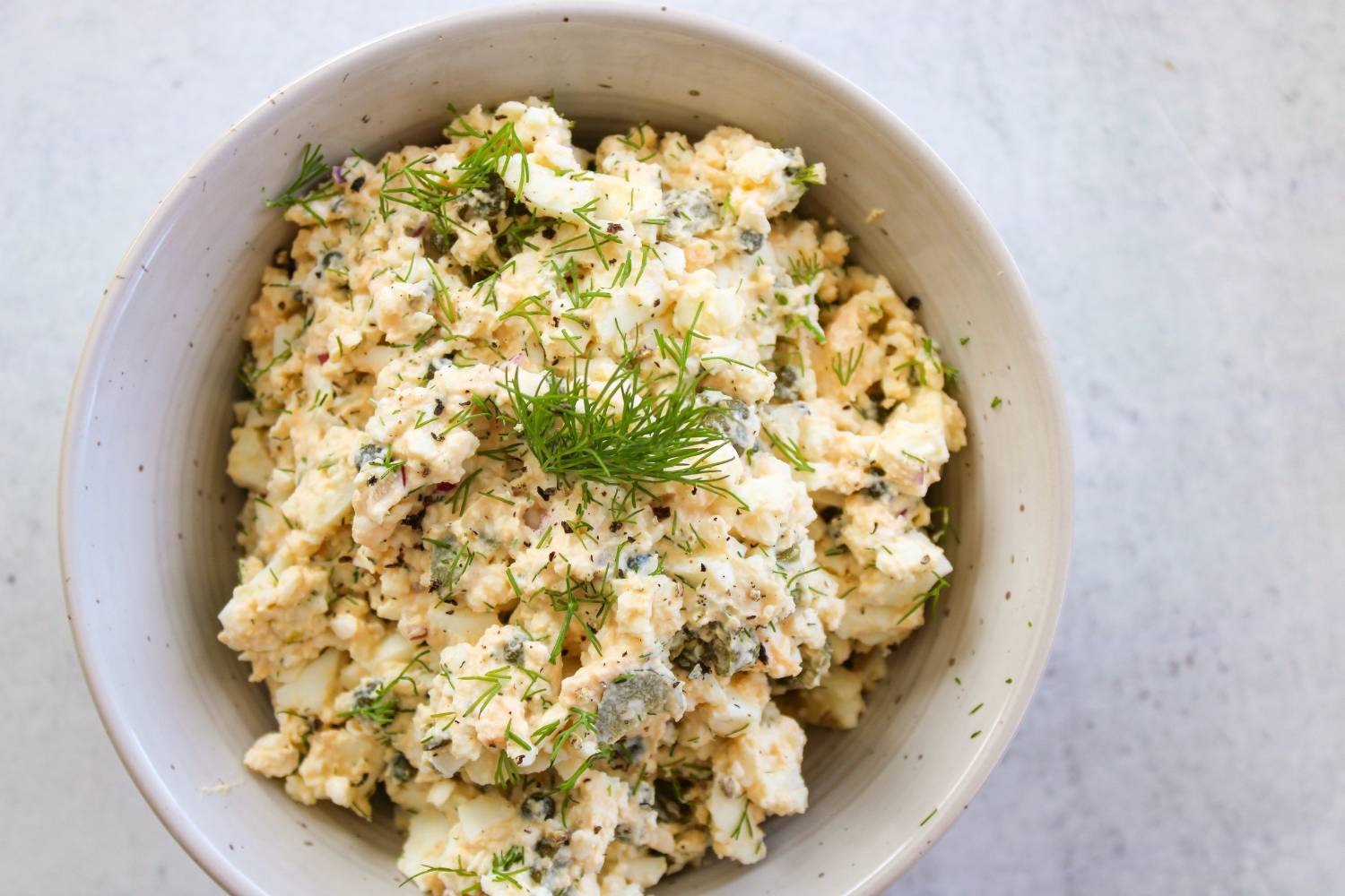 Egg salad in a small bowl with dill on top