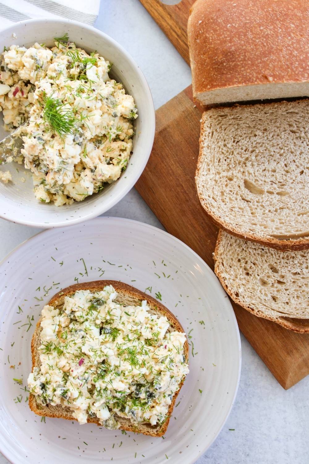 Small bowl of egg salad with a piece of toast and loaf of bread