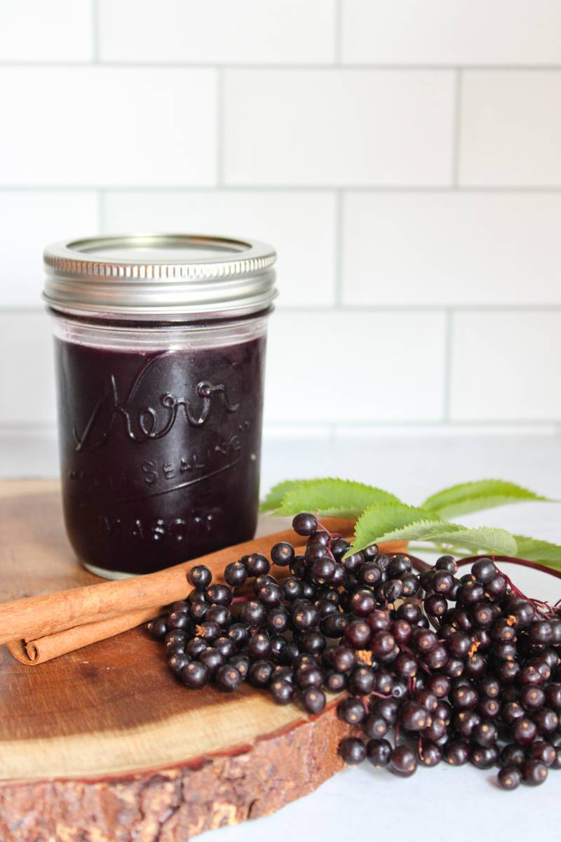 Elderberry Syrup in a mason jar next to fresh elderberries