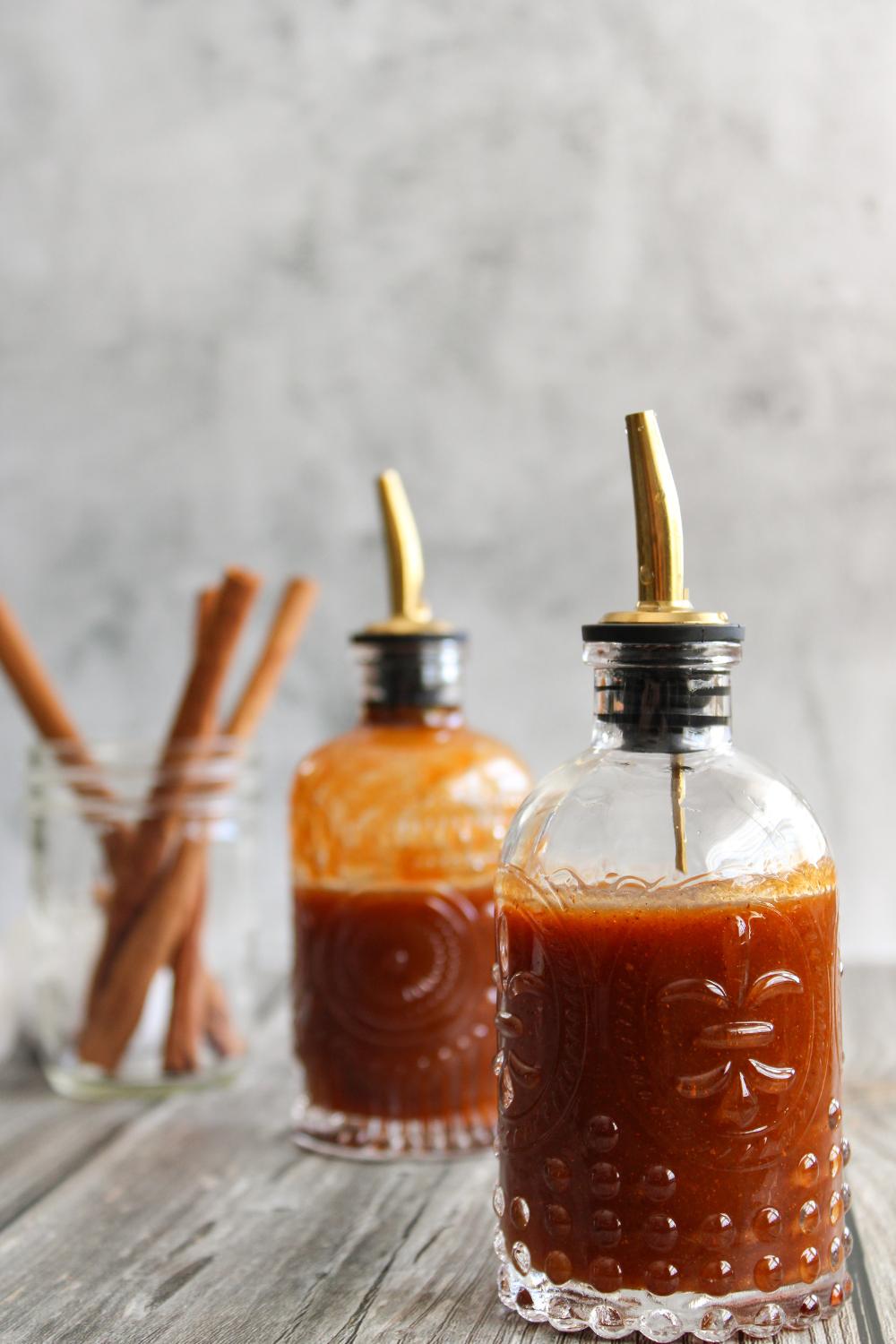 two bottles of pumpkin spice syrup with cinnamon sticks in the background