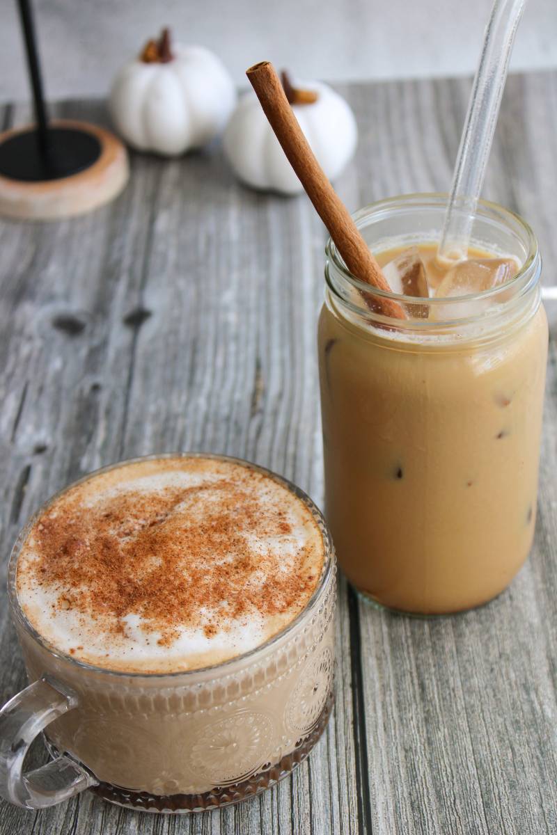 Hot pumpkin spice latte in a clear mug and an iced pumpkin spice latte in a jar