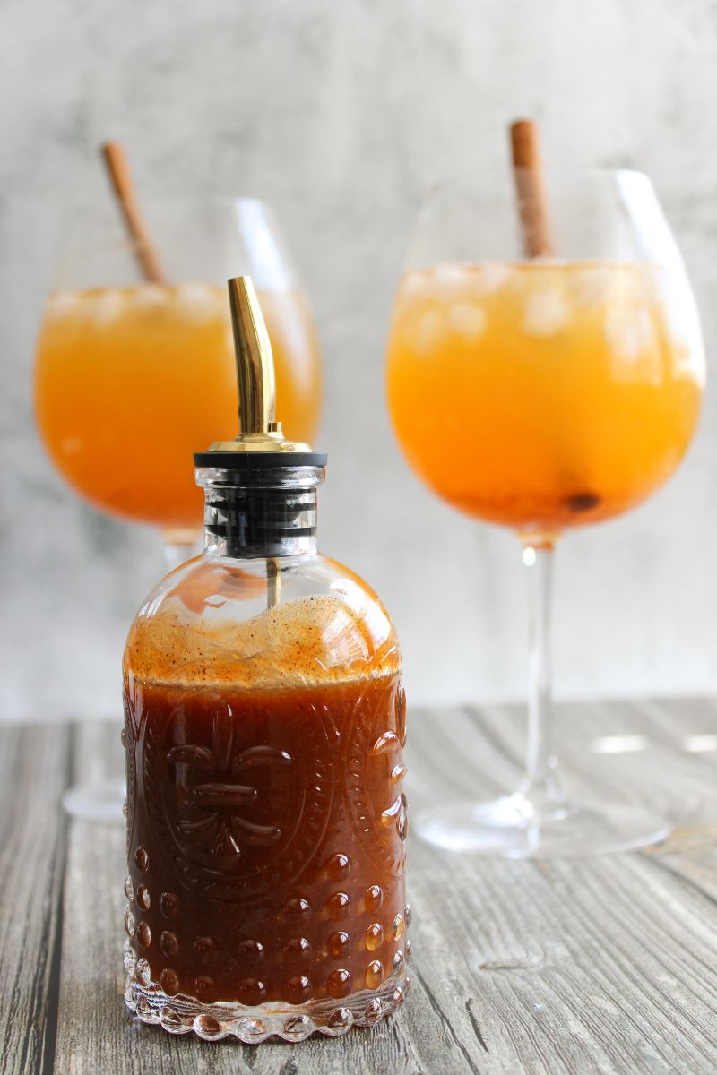 Pumpkin spice syrup in front of two Pumpkin Ginger Spice Mocktails