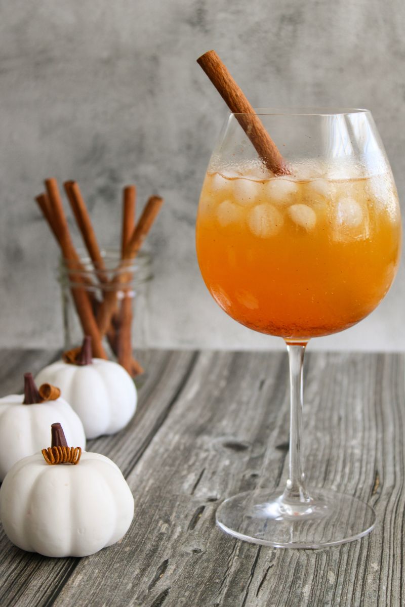 Wine glass filled with fall mocktail next to mini white pumpkins