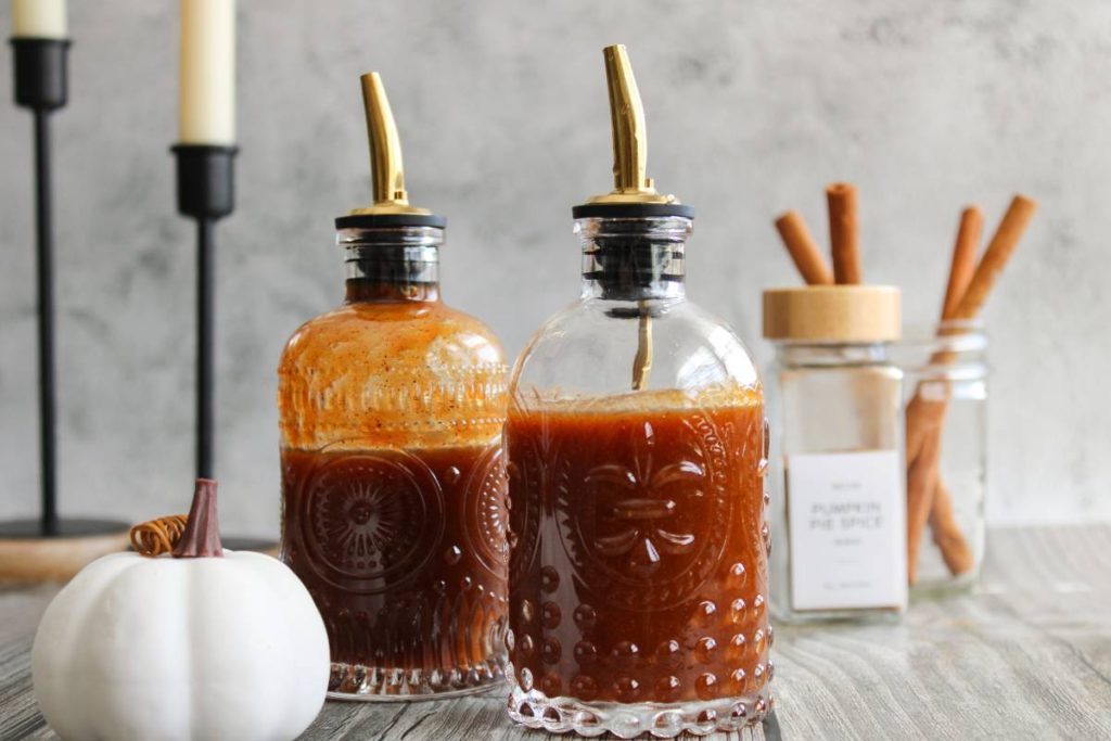 Two bottles of pumpkin spice syrup next to a white pumpkin and candle sticks