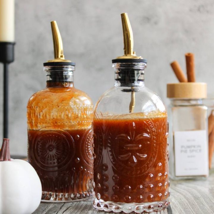 Two bottles of pumpkin spice syrup next to a white pumpkin and candle sticks