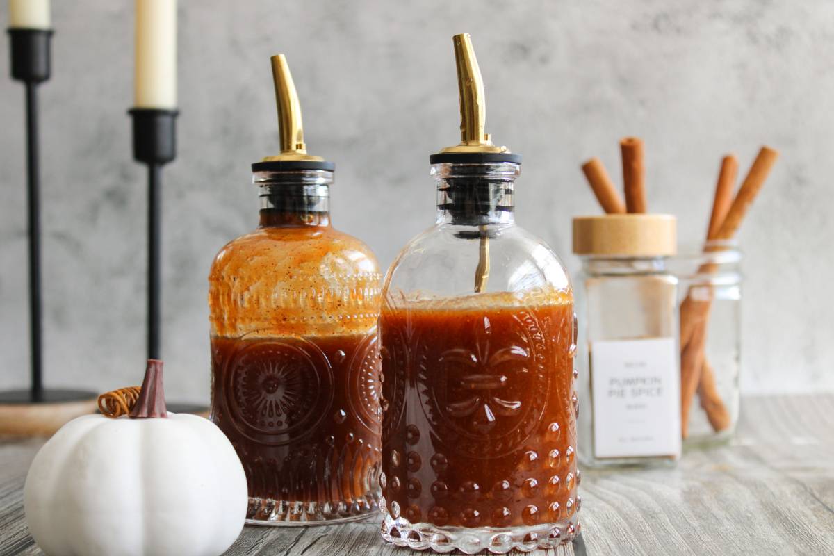 Two bottles of pumpkin spice syrup next to a white pumpkin and candle sticks 