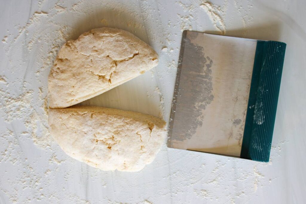 Pie crust dough cut in half with bench scraper