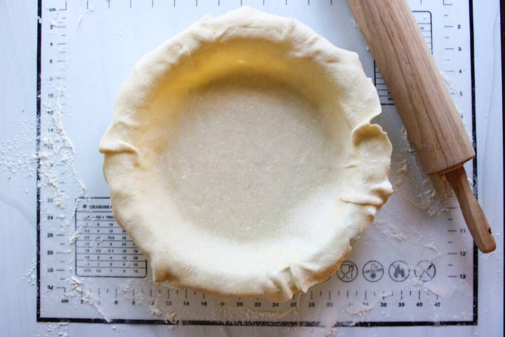 Pie crust in a pie pan with a rolling pin next to it