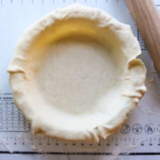 Pie crust in a pie pan with a rolling pin next to it