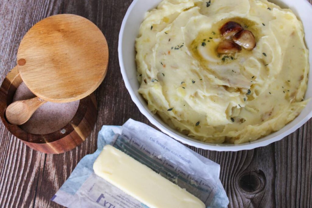 Bowl of mashed potatoes next to butter and salt