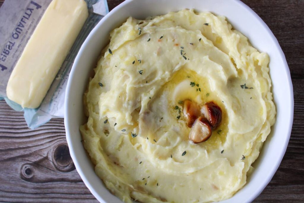 Bowl of mashed potatoes with a stick of butter next to it 