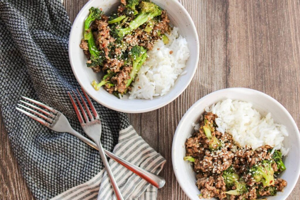 overhead view of ground beef and broccoli with two forks and a cloth napkin