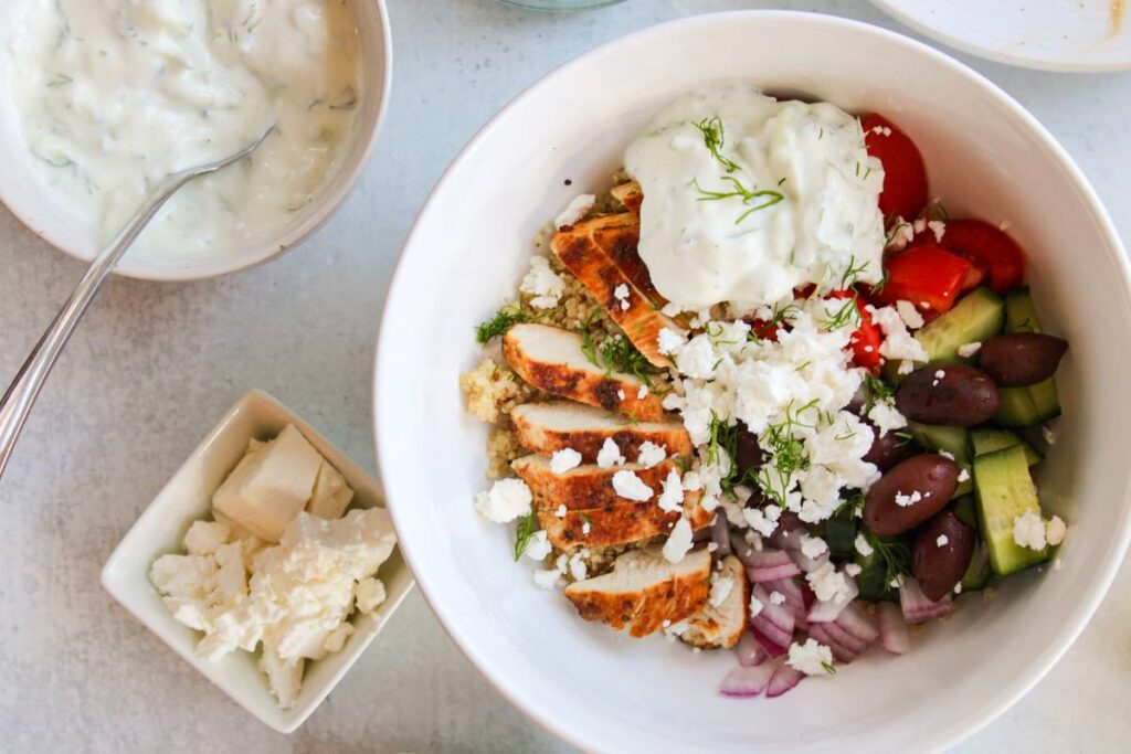 Greek Chicken Quinoa Bowls next to feta cheese and tzatziki.