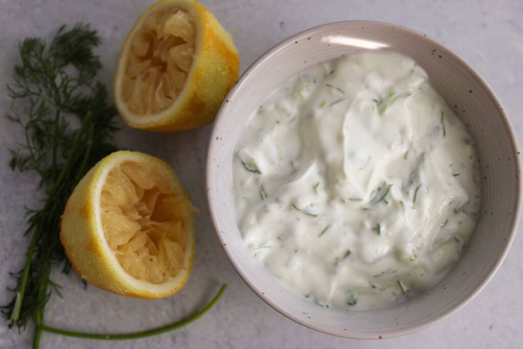 small bowl of tzatziki next to a lemon and dill