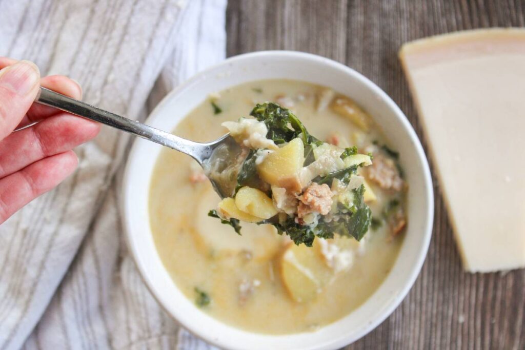 hand holding a spoon full of Zuppa Toscana Soup over a bowl