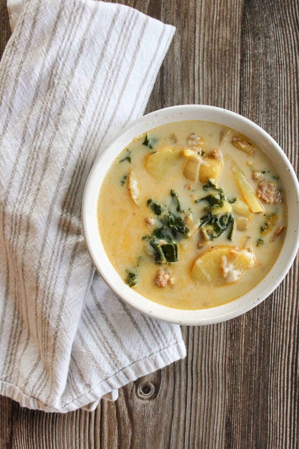 bowl of Zuppa Toscana Soup next to a white and grey napkin