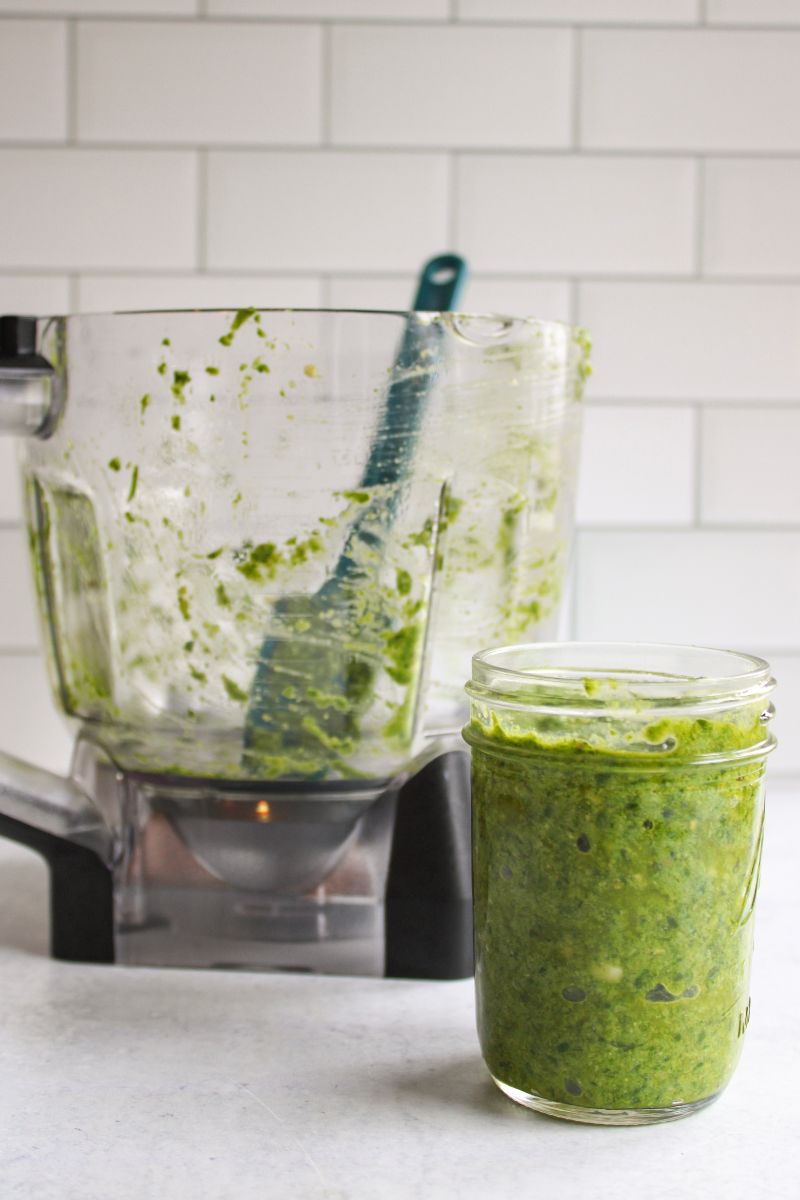 small mason jar filled with hazelnut pesto next to an empty food processor.