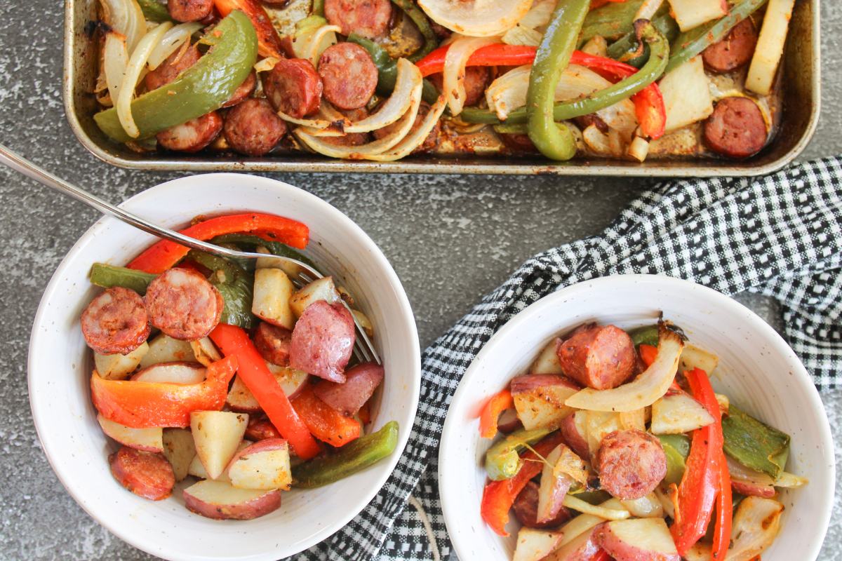 two bowls filled with Cajun Sausage, Potato and Vegetables next to a sheet pan