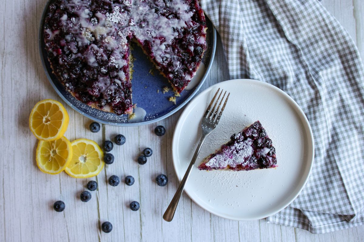 Blueberry lemon upside down cake on a blue plate with a slice of the cake on a white plate.