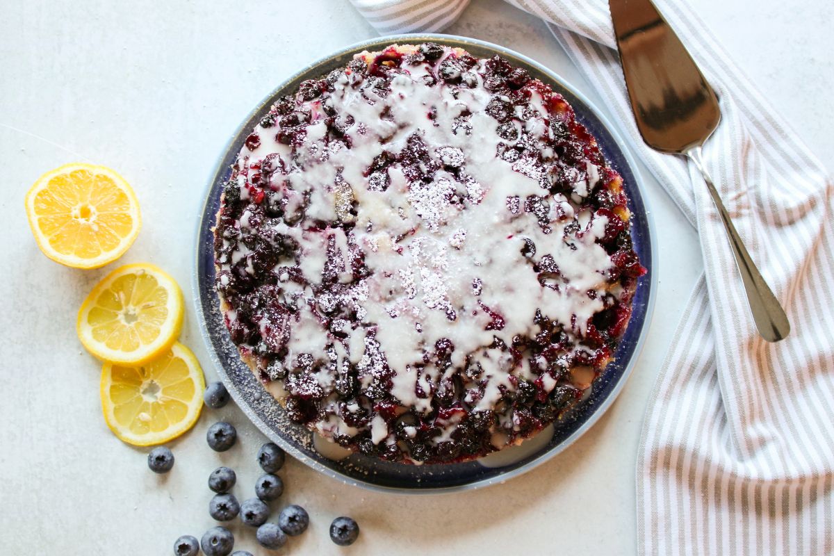 Blueberry Upside Down Cake on a blue plate next to lemon slices and blueberries