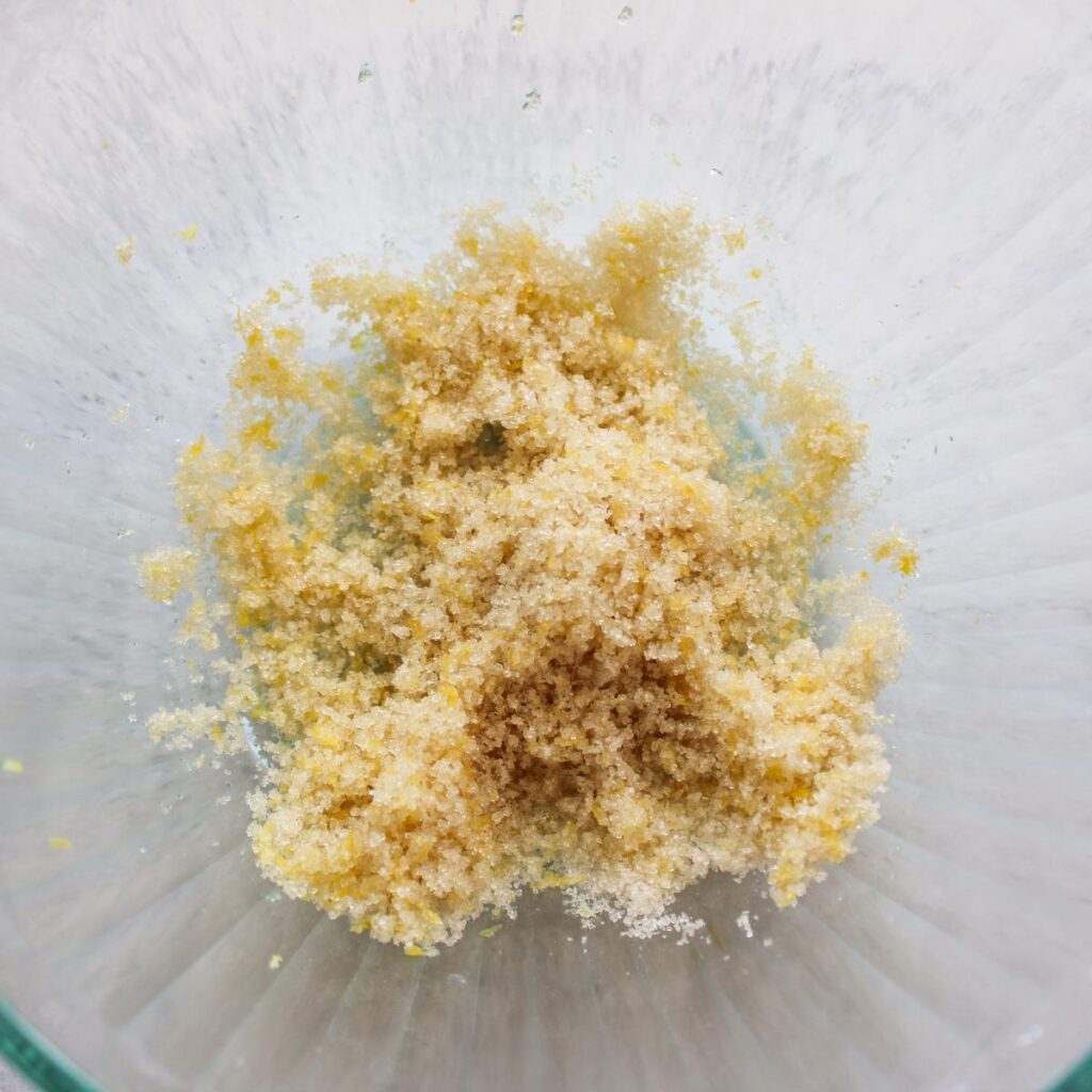 Sugar and lemon zest rubbed together in a clear bowl.