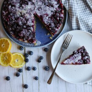 Blueberry lemon upside down cake on a blue plate with a slice of the cake on a white plate.