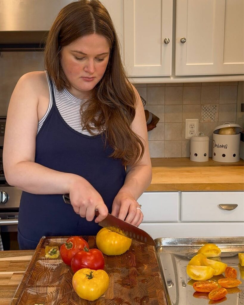 Slicing large tomatoes into chunks to add to a sheet pan.