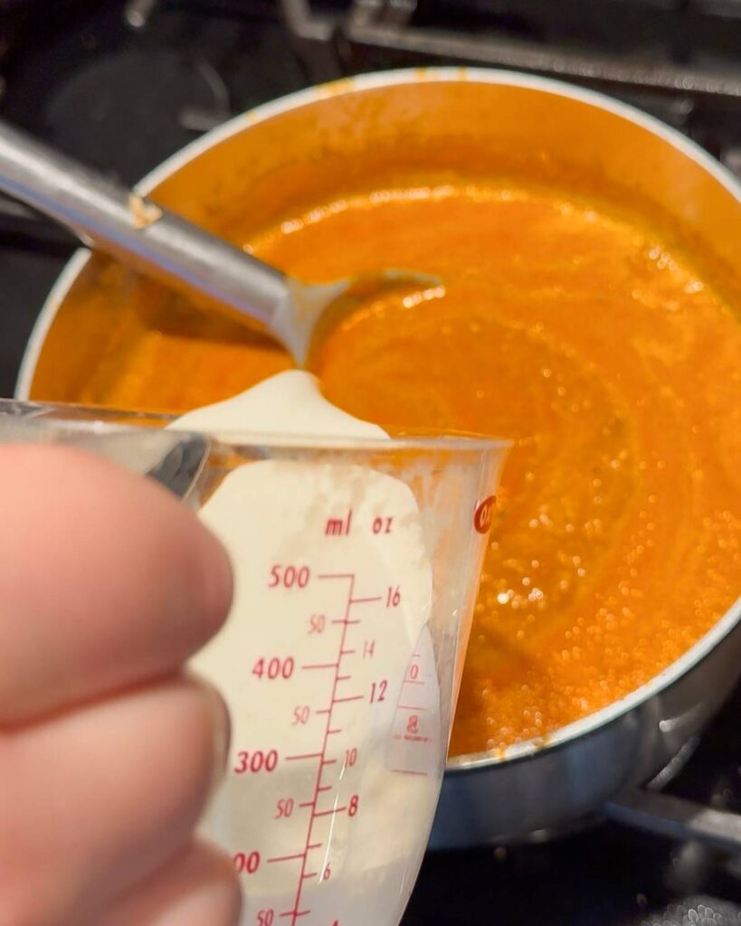 Heavy cream pouring into the Roasted Tomato Soup.