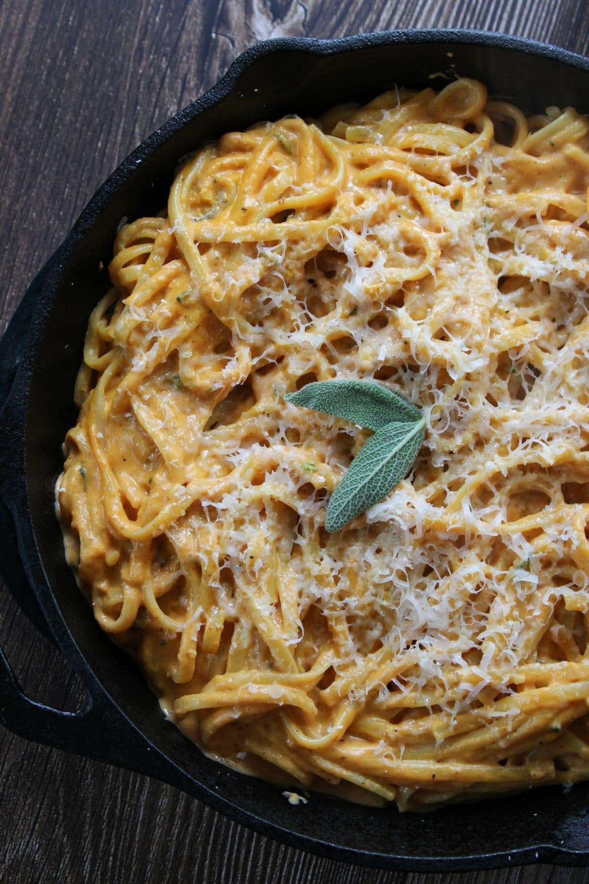 Creamy Pumpkin Pasta in a cast iron pan with parmesan and sage leaves on top.