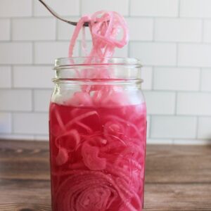 quick-pickled red onions in a quart mason jar with a fork pulling some onions out.