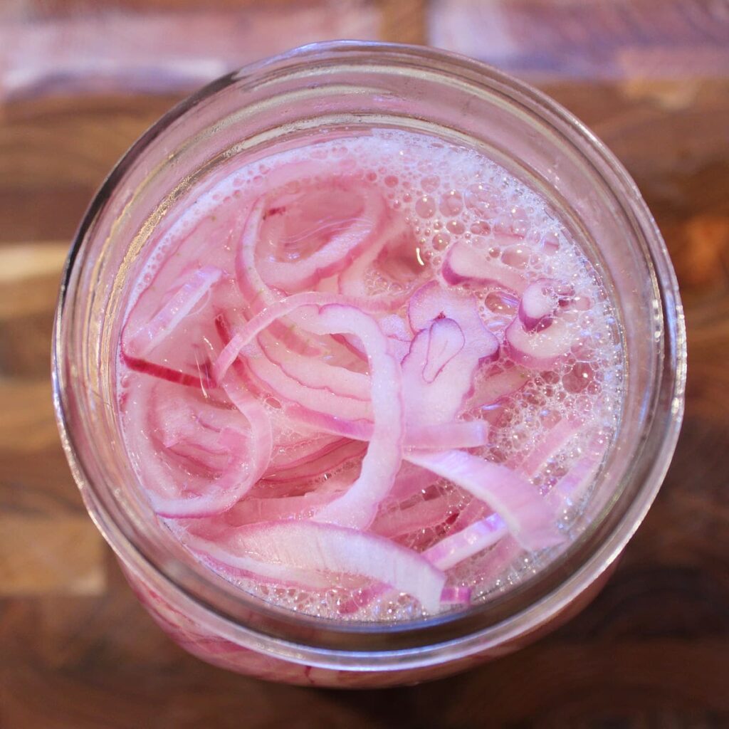 Overhead view of red onions in a mason jar with hot brine poured over top.