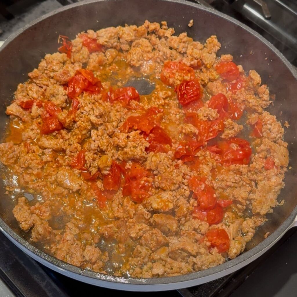 Tomatoes and seasoning in with the Italian sausage in a skillet for High Protein Pasta.