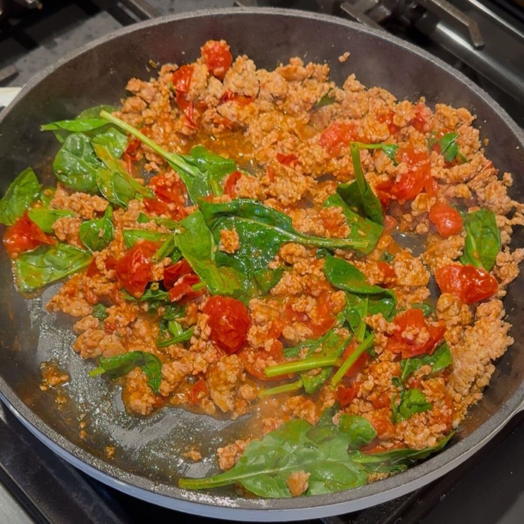 Spinach added to tomato and sausage mixture for high protein pasta.