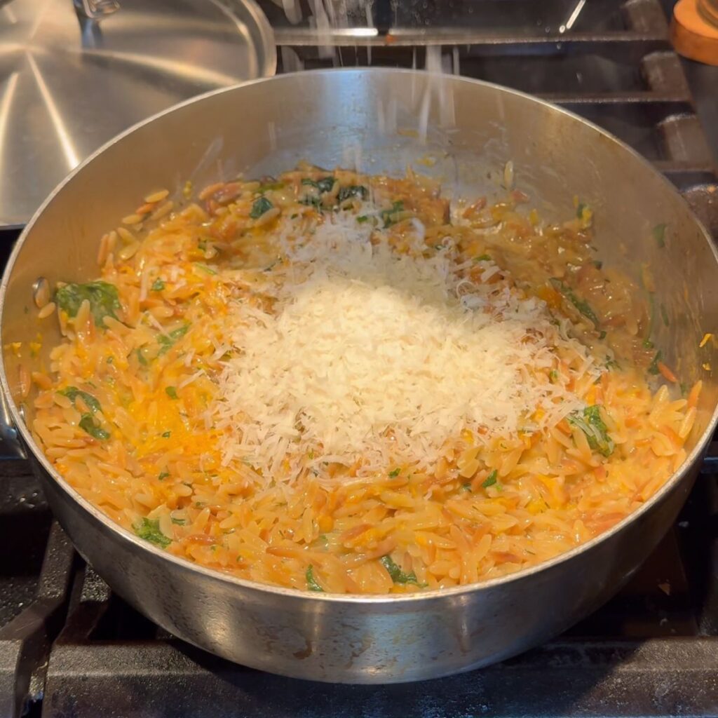 Parmesan cheese added to the creamy orzo in a medium pan.