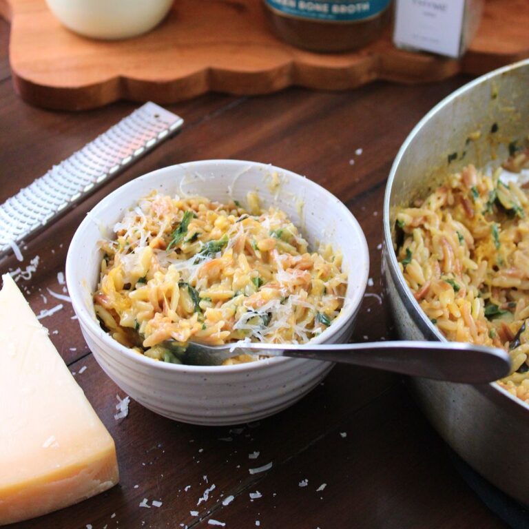 A bowl of creamy orzo next to a saucepan filled with creamy orzo next to Parmesan cheese.