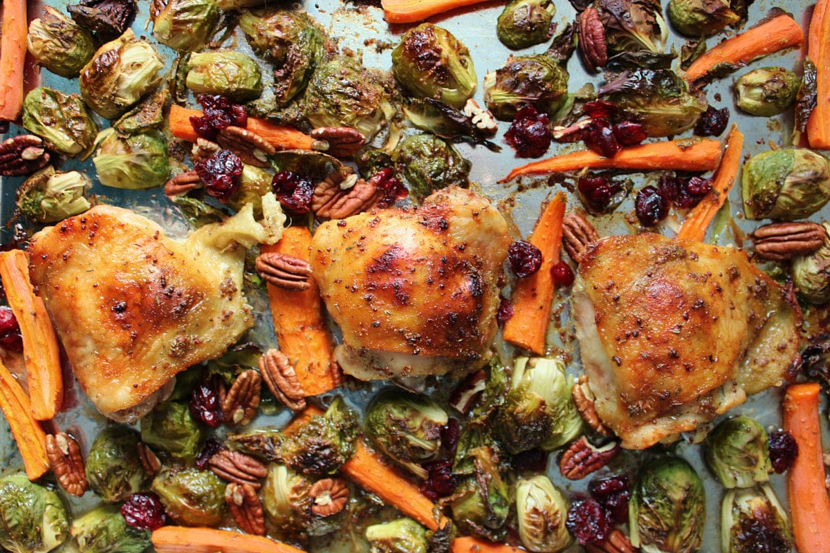 Crispy chicken thighs with caramelized Brussels sprouts and carrots tossed in a maple mustard sauce with pecans and dried cranberries on a sheet pan.