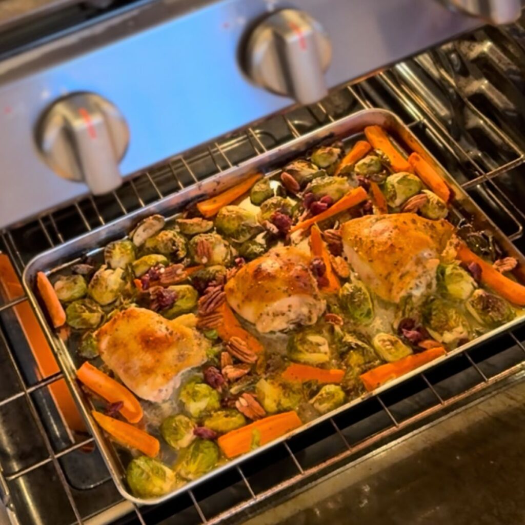 Crispy chicken thighs with caramelized Brussels sprouts and carrots tossed in a maple mustard sauce with pecans and dried cranberries on a sheet pan in the oven.